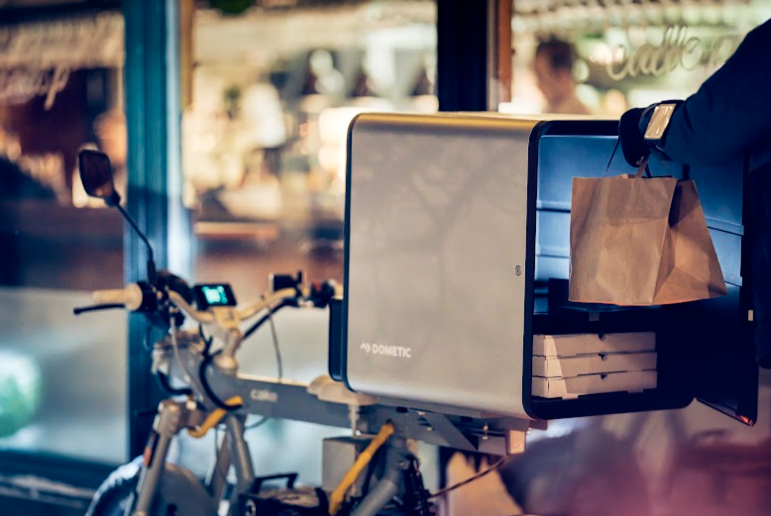 A close up image of a bike with a Dometic DeliBox on the back. The DeliBox is open and stocked with boxes and bags.