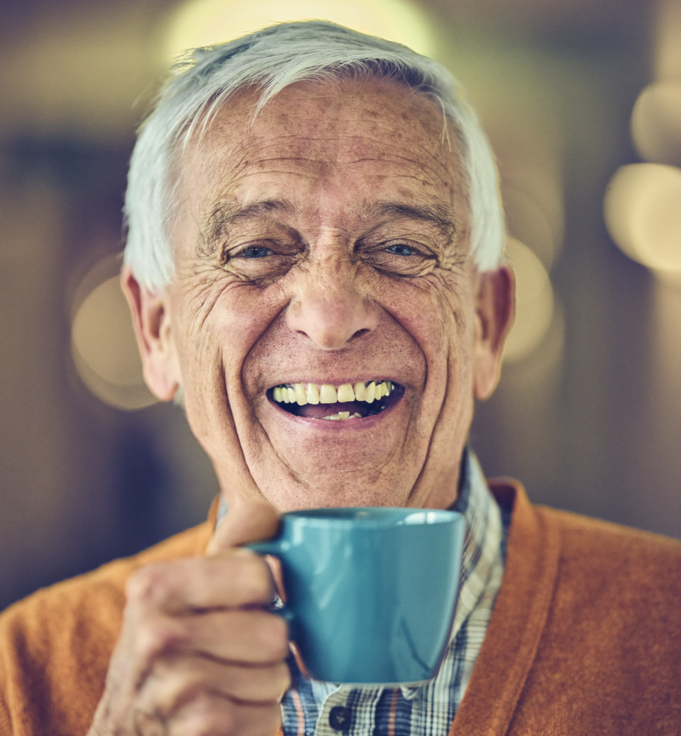 Elderly man smiling with a cup of coffee in his hand