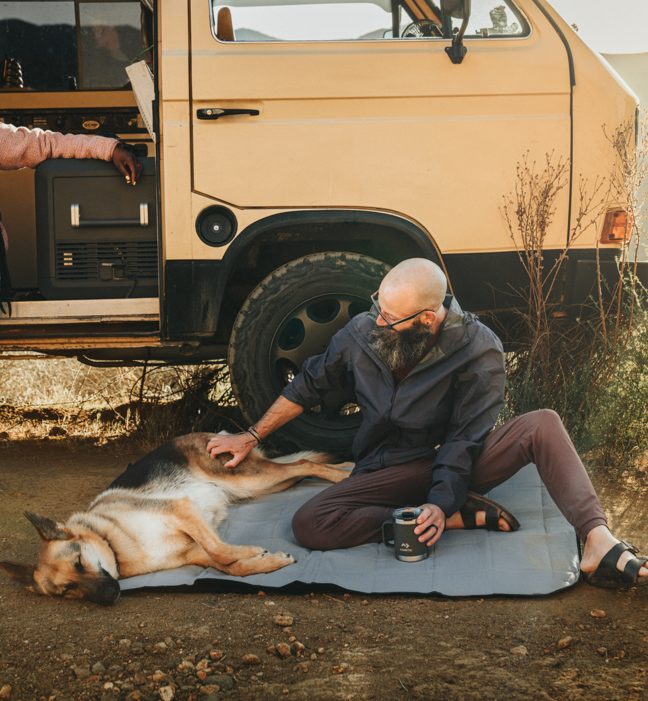 man sitting with dog on Dometic blanket while camping