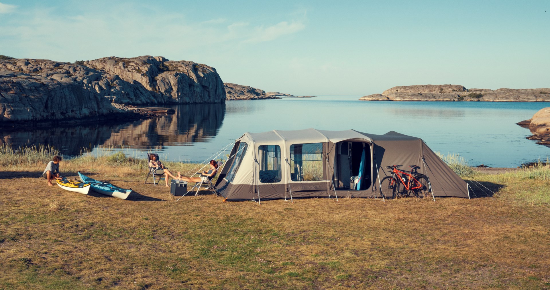 Couple se relaxant devant une tente en bord de mer avec du matériel de camping Dometic, dont une glacière à compresseur CFX et du mobilier de camping.
