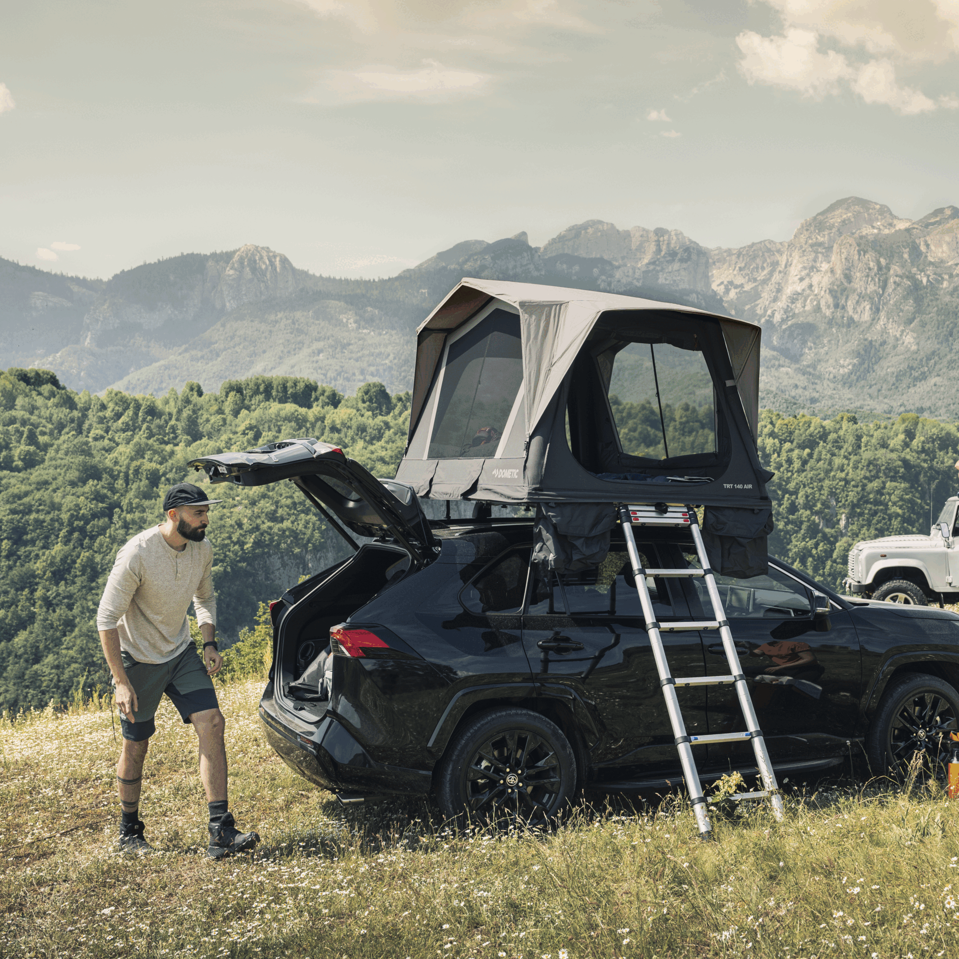 Mann richtet das Camp neben einem schwarzen SUV mit Dometic Dachzelt in den Bergen ein – ideal für Overlanding und Dachzelt-Abenteuer